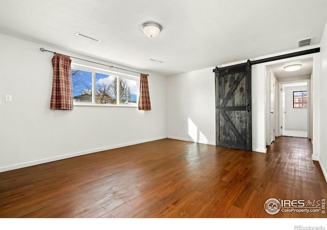 spare room featuring a barn door, wood finished floors, visible vents, and baseboards