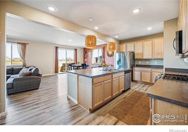 kitchen featuring dark countertops, open floor plan, stainless steel appliances, light brown cabinets, and a sink