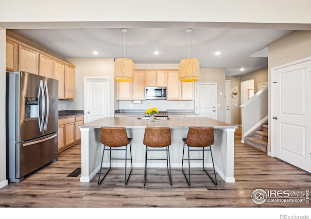 kitchen with a breakfast bar, dark wood-style flooring, appliances with stainless steel finishes, light brown cabinetry, and an island with sink