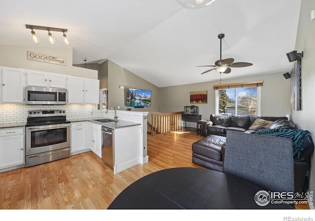 kitchen featuring open floor plan, a peninsula, stainless steel appliances, white cabinetry, and a sink