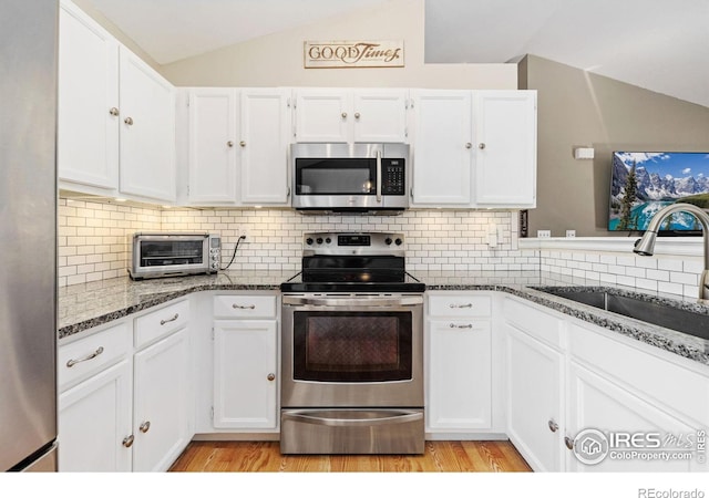 kitchen with a toaster, white cabinets, vaulted ceiling, stainless steel appliances, and a sink