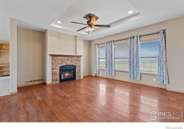 unfurnished living room featuring visible vents, a ceiling fan, wood finished floors, a tray ceiling, and a fireplace