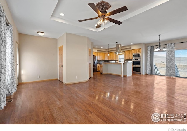 unfurnished living room with a tray ceiling, wood finished floors, a ceiling fan, and baseboards