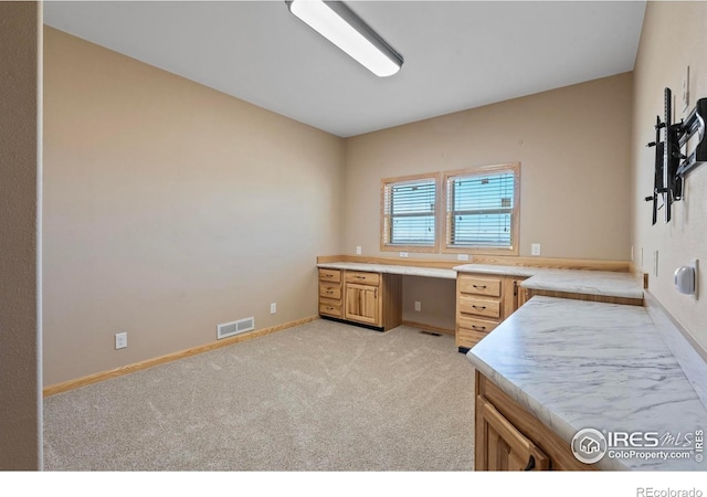 home office featuring visible vents, light colored carpet, built in desk, and baseboards