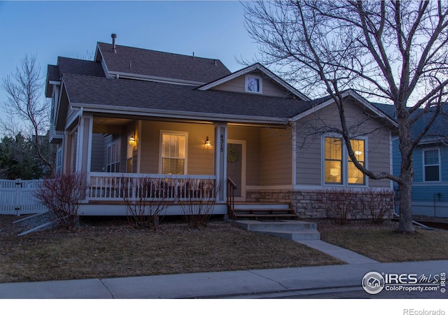 bungalow-style house featuring covered porch, stone siding, fence, and roof with shingles