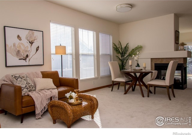 living room with a wealth of natural light, baseboards, a tiled fireplace, and light colored carpet