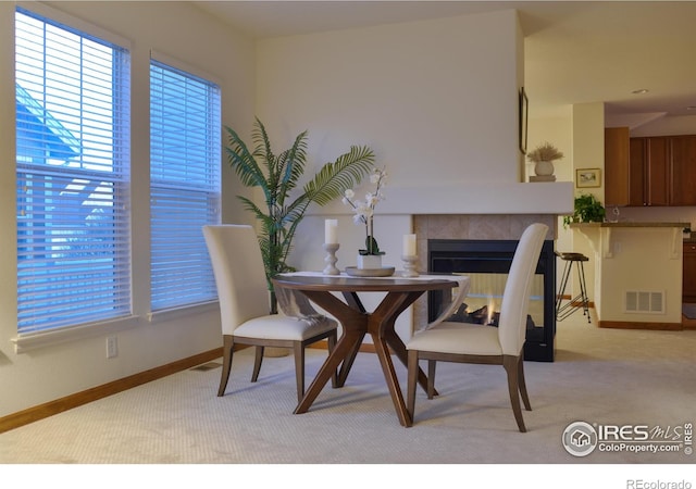 dining space featuring baseboards, a tile fireplace, visible vents, and light colored carpet