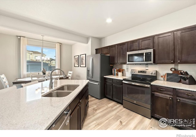 kitchen with light stone counters, a sink, light wood-style floors, dark brown cabinets, and appliances with stainless steel finishes