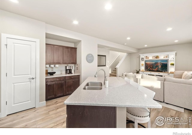 kitchen featuring an island with sink, light stone counters, open floor plan, light wood-style floors, and a sink