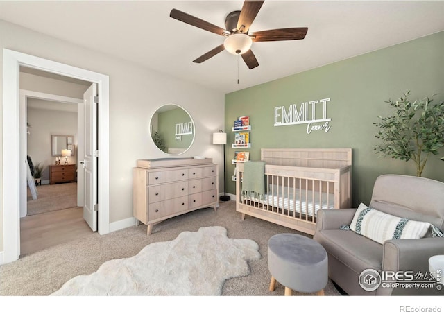 carpeted bedroom featuring ceiling fan, a crib, and baseboards