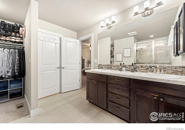 full bathroom featuring double vanity, a stall shower, decorative backsplash, and a sink