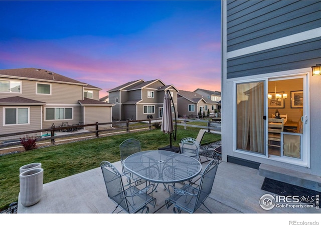 patio terrace at dusk featuring outdoor dining space, a lawn, a residential view, and fence