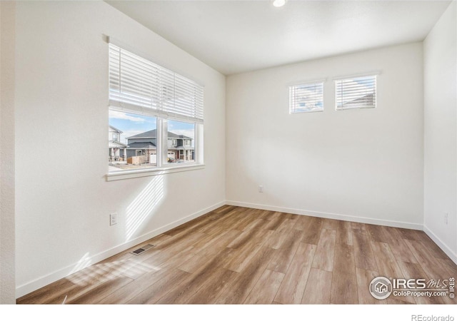 spare room with wood finished floors, visible vents, and baseboards