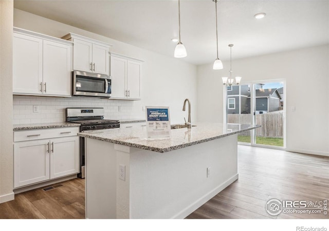 kitchen with appliances with stainless steel finishes, wood finished floors, a sink, and tasteful backsplash