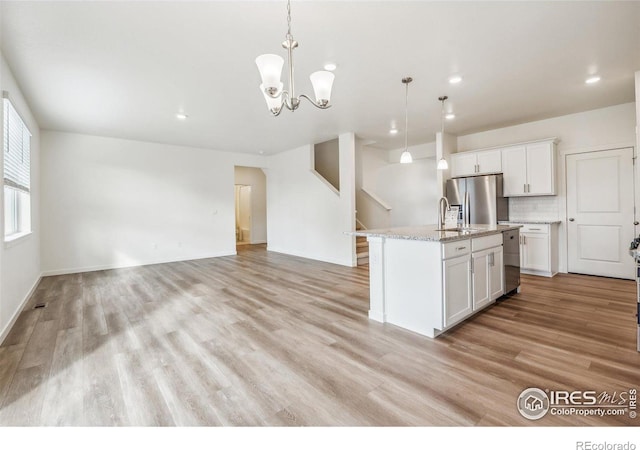 kitchen with pendant lighting, a center island with sink, appliances with stainless steel finishes, white cabinets, and light wood-type flooring