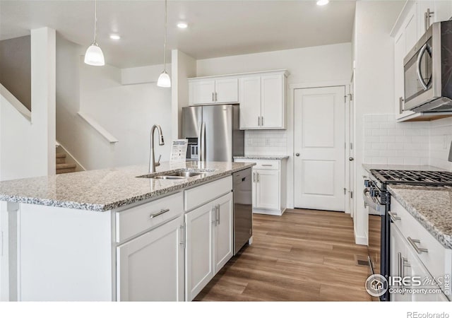 kitchen featuring white cabinets, an island with sink, light wood-style flooring, appliances with stainless steel finishes, and a sink