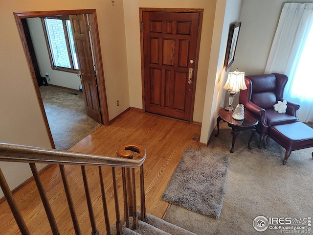 foyer entrance with light carpet, stairway, light wood-style flooring, and baseboards