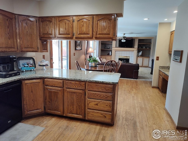 kitchen with black dishwasher, a peninsula, a fireplace, and light wood-style floors