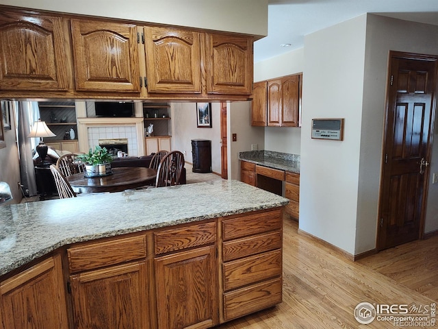 kitchen with light wood-style floors, brown cabinets, a tiled fireplace, and light stone countertops