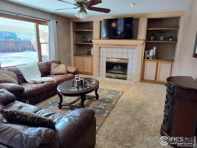 living area with light carpet, built in shelves, a tile fireplace, and a ceiling fan