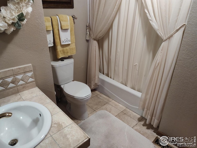 full bath featuring shower / tub combo with curtain, a textured wall, toilet, a sink, and tile patterned floors