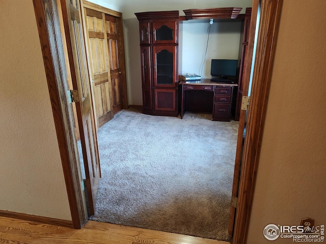 unfurnished office with light carpet, a textured wall, and baseboards