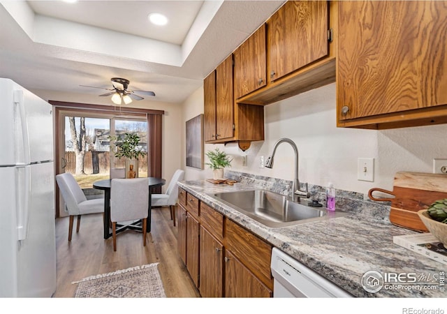 kitchen with brown cabinets, a ceiling fan, a sink, light wood-type flooring, and white appliances