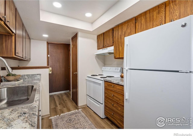 kitchen featuring light wood-style flooring, brown cabinetry, a sink, white appliances, and under cabinet range hood