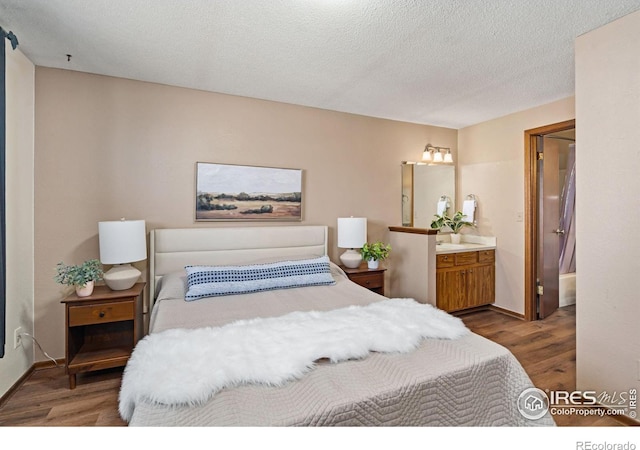 bedroom with a textured ceiling, baseboards, wood finished floors, and ensuite bathroom