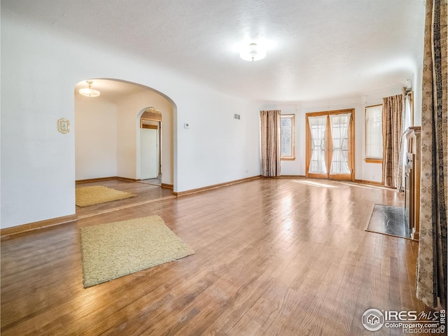 spare room with baseboards, arched walkways, and wood finished floors