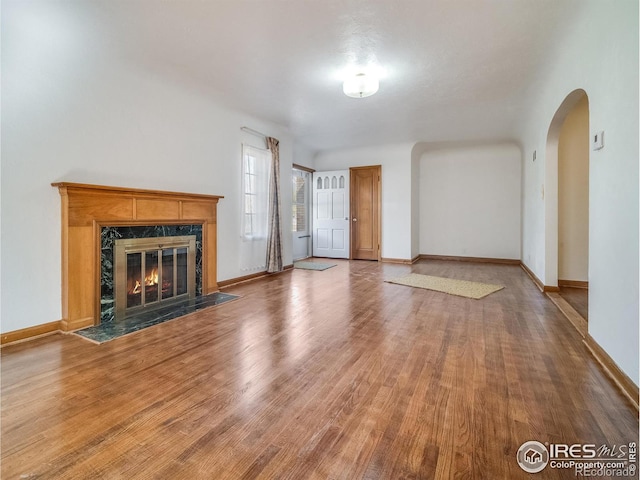 unfurnished living room featuring baseboards, a fireplace, arched walkways, and wood finished floors