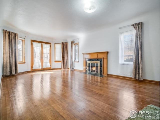 unfurnished living room with french doors, a premium fireplace, wood finished floors, and baseboards