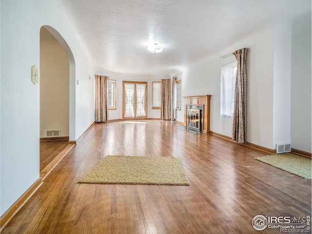 unfurnished living room featuring a fireplace with flush hearth, arched walkways, wood finished floors, and visible vents