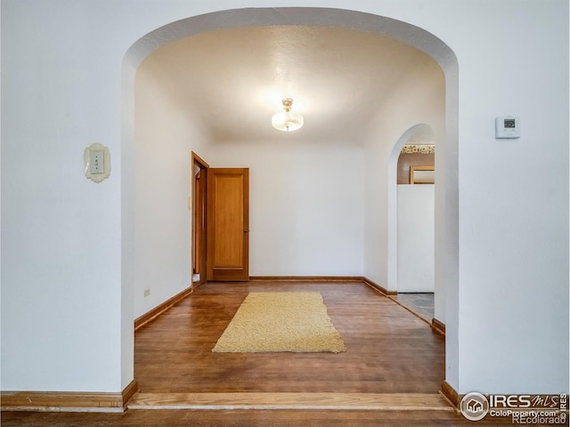 hall with baseboards, arched walkways, and wood finished floors