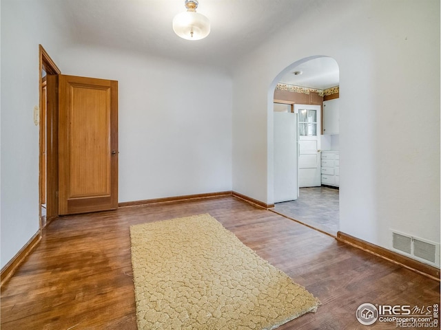 empty room with baseboards, visible vents, arched walkways, and wood finished floors