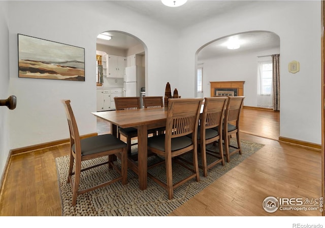 dining area featuring arched walkways, a fireplace, wood finished floors, and baseboards