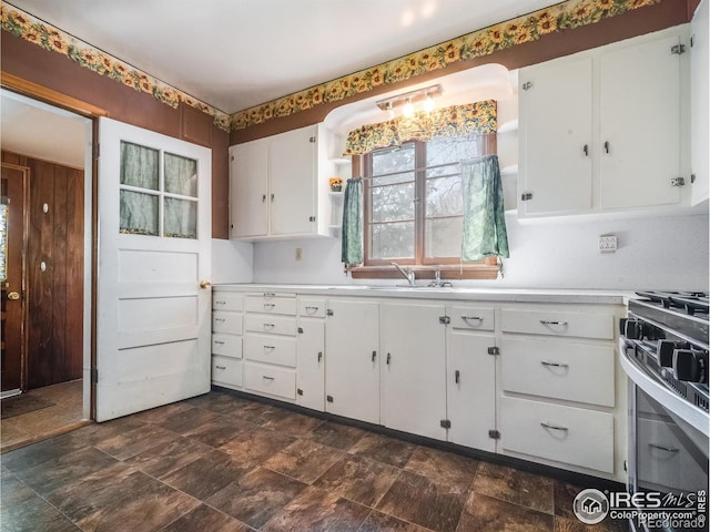 kitchen with stainless steel range with gas stovetop, light countertops, a sink, and white cabinetry