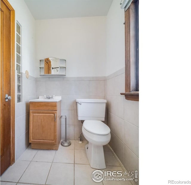 half bath with a wainscoted wall, tile walls, toilet, and tile patterned floors