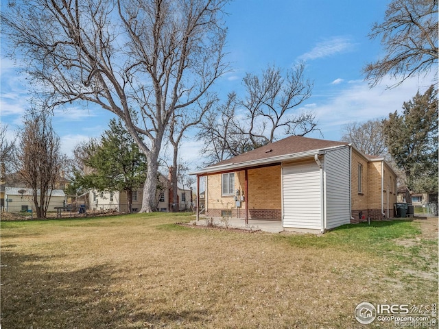 rear view of property with crawl space, brick siding, a lawn, and a patio