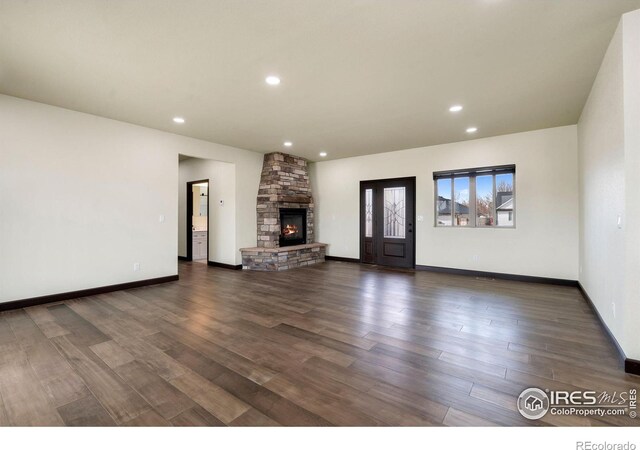 unfurnished living room featuring recessed lighting, baseboards, a stone fireplace, and dark wood-style floors