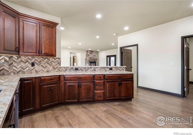 kitchen featuring light stone counters, decorative backsplash, recessed lighting, light wood-style flooring, and a peninsula