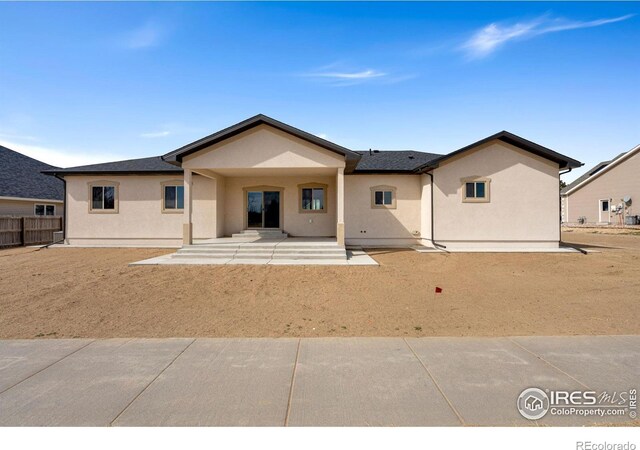 rear view of house featuring stucco siding and fence