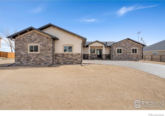 back of house featuring stone siding, stucco siding, and fence