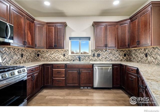 kitchen featuring appliances with stainless steel finishes, light stone countertops, light wood-type flooring, and a sink