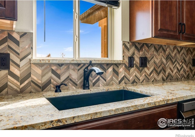 kitchen with light stone counters, tasteful backsplash, dark brown cabinets, and a sink