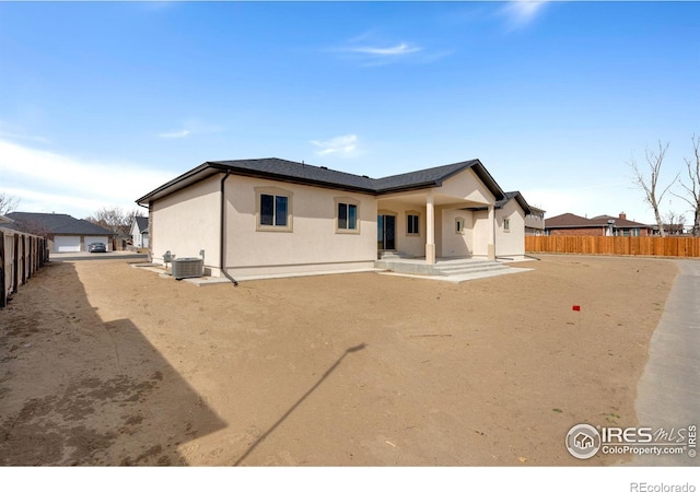 rear view of property featuring stucco siding, central AC unit, and fence