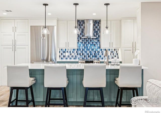 kitchen with visible vents, white cabinets, wall chimney range hood, stainless steel refrigerator, and decorative backsplash