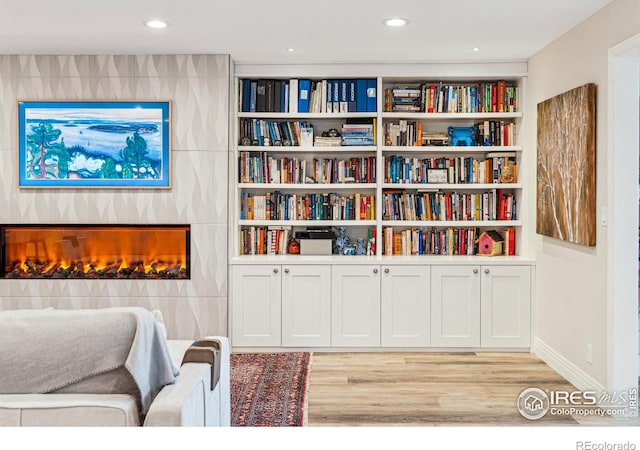 sitting room featuring a warm lit fireplace, light wood finished floors, built in features, and recessed lighting