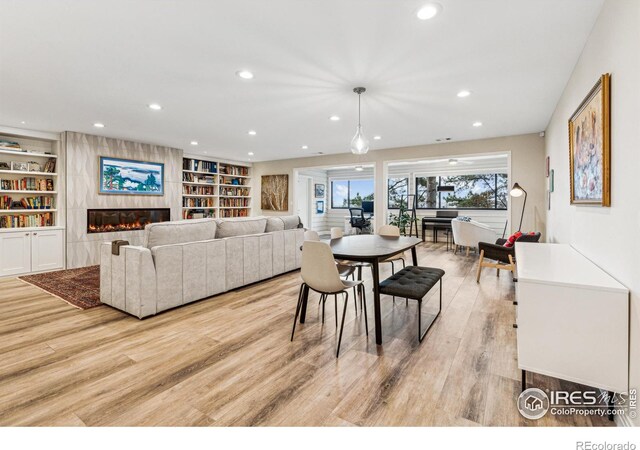 dining space featuring built in shelves, a high end fireplace, light wood finished floors, and recessed lighting