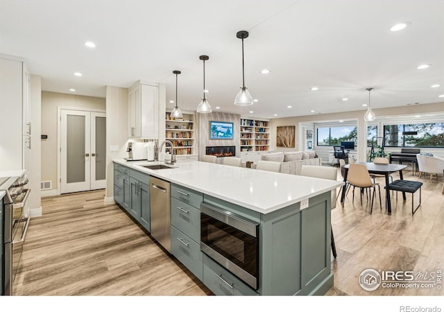 kitchen featuring a large fireplace, a sink, white cabinets, french doors, and appliances with stainless steel finishes